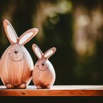 Two adorable wooden bunny figurines with happy faces on a table against a blurred outdoor background.